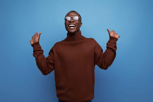 elegant young african brunet male businessman in stylish brown sweater and glasses on studio background with copy space.