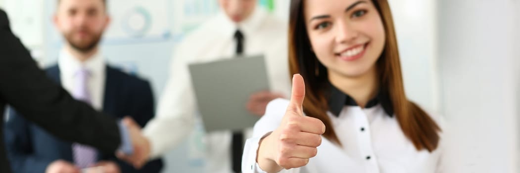 Businesswoman feels confident in team and thumbs up gesture. Happy businesswoman showing thumbs up and smiling colleagues standing in background