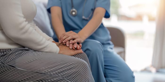 Doctor giving hope. Close up shot of young female physician leaning forward to smiling elderly lady patient holding her hand in palms. Woman caretaker in white coat supporting encouraging old person.