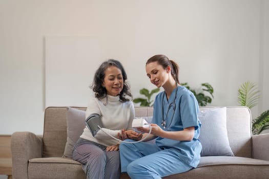 nurse doctor using digital tonometer check blood pressure for old asia female at home in elderly care cardiovascular medical visit, cholesterol problem. Home health care and nursing home concept.