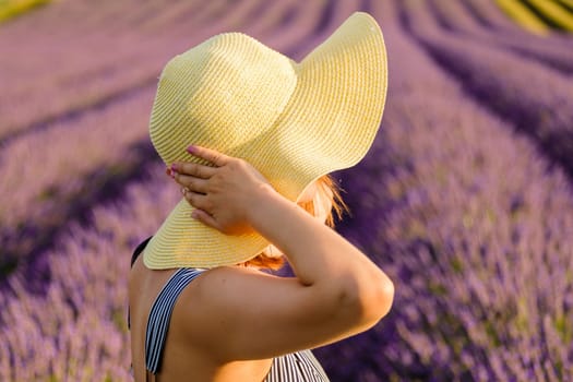 A young lady wearing a straw hat standing in the captivating sight of a lavender field.