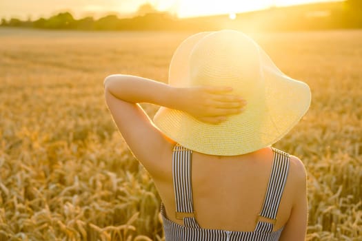 Woman holding a straw hat and enjoying the sunset in the wheat field.