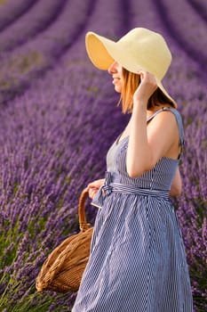 A young lady, adorned with a straw hat, delightfully stands in lavender field, gracefully carrying a wicker basket filled with vibrant violet blooms.