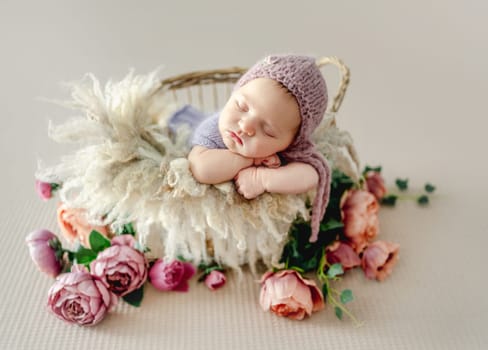 Newborn baby girl sleeping on fur and peony flowers. Cute infant child kid napping in basket studio portrait