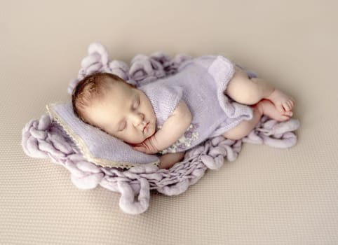 Newborn baby girl sleeping on knitted pillow and blanket. Cute infant child kid napping and holding hands under cheek in studio