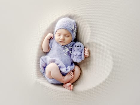 Newborn baby girl wearing dress sleeping in heart shape basket with toy. Cute infant child kid in wreath napping on fur