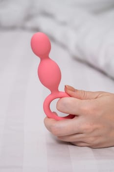 Close-up of a female hand with pink anal beads lying in bed