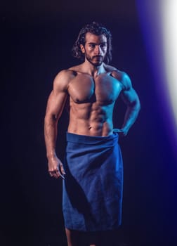 Portrait of naked handsome man with languishing look covering with a towel, against dark background