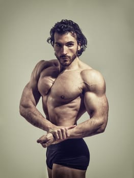Handsome male bodybuilder doing classic bodybuilding pose, looking at camera, on light background