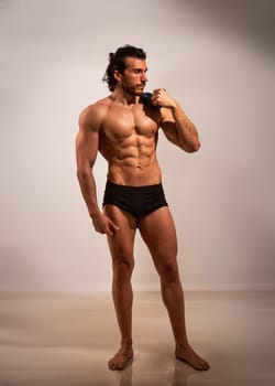 Handsome male bodybuilder doing classic ancient statue pose, looking away, on light background