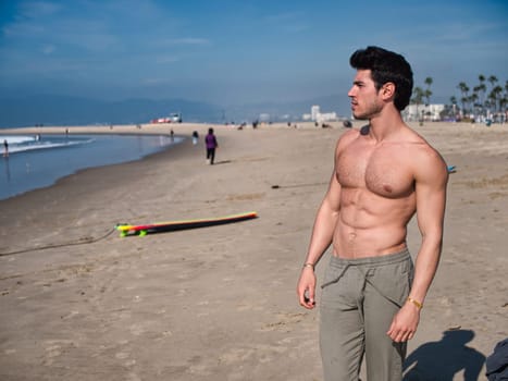 Handsome young man standing on a beach, shirtless wearing boxer shorts, showing muscular fit body in Venice Beach, California, USA