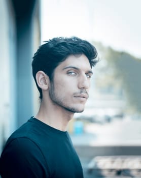 Head and shoulders shot of one handsome young man with green eyes in urban setting, looking at camera, wearing t-shirt