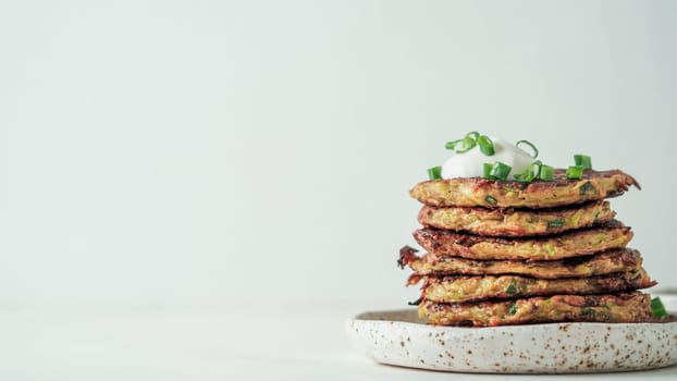 Gluten free zucchini fritters in stack on white background. Zucchini pancakes or fritters with green onion and parmesan cheese, served sour cream or greek yogurt Banner. Copy space