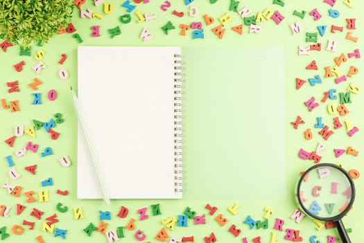 Open notebook with a pencil and a magnifying glass on a green background. Top view. Colored wooden alphabet on a school desk. Flat lay. Back to school concept.