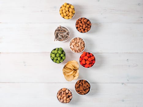 Assortment of different snack for beer, wine, party. Peanuts in coconut glaze, green vasabi, red spicy chilli, yellow cheese glaze, chips, pistachio, crackers, fish on white wooden table. Copy space
