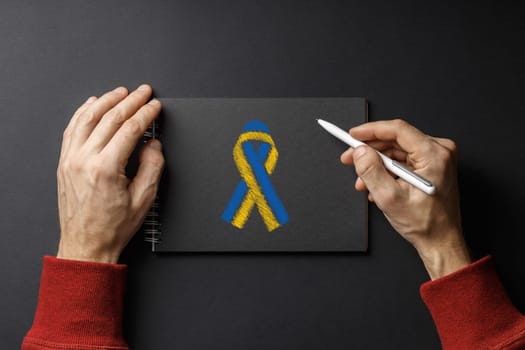 I am writing letter, pen in my hands and yellow blue ribbon on black notepad on black background. concept needs help and support, truth will win