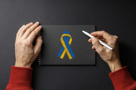 I am writing letter, pen in my hands and yellow blue ribbon on black notepad on black background. concept needs help and support, truth will win