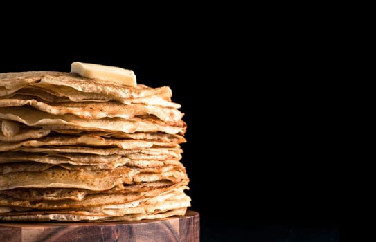 Stack of traditional russian pancakes blini isolated on black background with copy space. Homemade russian thin pancakes blini with butter piece. Russian food, russian kitchen