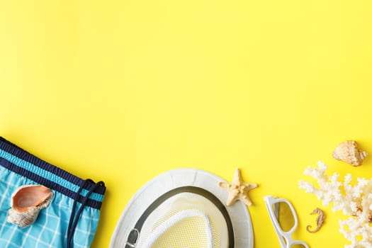 Beach hat with shorts and sunglasses on a yellow isolated background. Flat lay. Summer vacation concept. Corals and seashells. Top view.