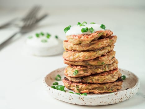 Zucchini fritters. Traditional zucchini fritters in stack on white background. Zucchini pancakes or fritters with green onion and parmesan cheese,served sour cream or greek yogurt. Copy space for text