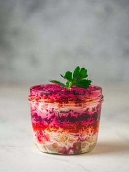 Layered salad herring under a fur coat on festive table, with fir tree and light garland. Traditional russian salad with herring and vegetables in glass jar. Copy space for text. Vertical.