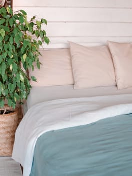 Bed in country house bedroom interior background. Green waringin tree near bed in scandinavian country house. Vertical. Copy space