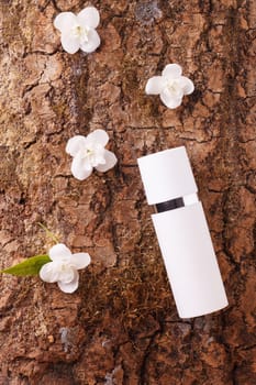 White plastic bottle with moisturizing face cream on tree bark with white jasmine flowers. The concept of bio-organic cosmetics with natural extract and vitamins