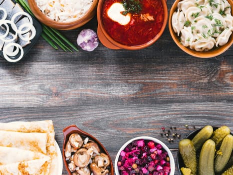 Russian food on wooden background. Assortment dishes of Russian cuisine - borscht, pelmeni, herring, marinated mushrooms, salted cucumbers, vinaigrette, sauerkraut and pancakes. Top view. Copy space.