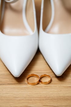 Golden rings of the newlyweds between white shoes with heels. Precious rings of the bride and groom