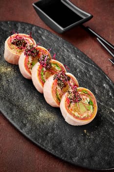 Set of delicious sushi rolls with tuna, japanese omelette, lettuce, avocado and orange wrapped in mamenori topped with caviar sprinkled with gold powder served on slate board with soy sauce