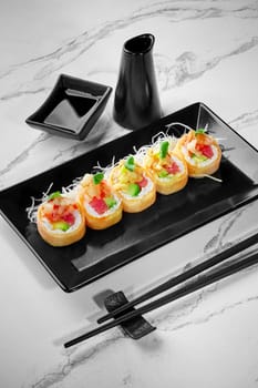 Set of appetizing rolls in mamenori filled with salmon, tuna, avocado topped with sea scallop in sweet chili sauce served with shredded daikon and soy sauce on black plate. Popular Japanese style dish