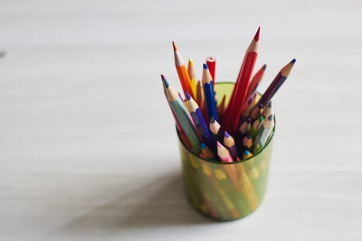 Photo of multi-colored wooden pencils in plastic cup on table. View from above. Learning, drawing, creativity and business.
