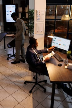 Businessman analyzing company investment profit progress report, typing marketing strategy on computer. African american entrepreneur working overhours at financial project. Business concept