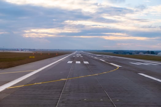 At the airport, endless runway extends into the horizon, featuring prominent aircraft markings and well-defined pathways for the safe arrival and departure of planes at sunset