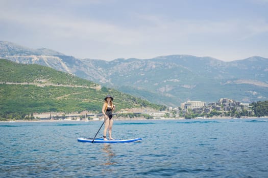 Young women Having Fun Stand Up Paddling in blue water sea in Montenegro. Against the backdrop of the Montenegrin mountains. SUP.