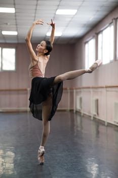 Graceful Asian ballerina in a beige bodysuit and black skirt is rehearsing in a dance class