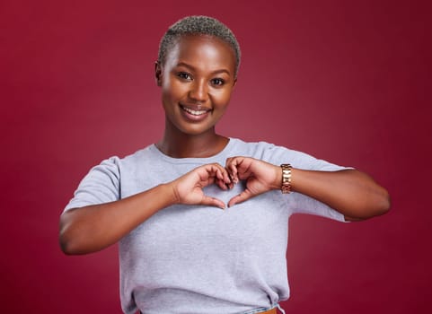 Hands, heart and love with a model black woman in studio on a red background to promote health or wellness. Portrait, smile and hand sign with a young female posing to endorse romance or cardio.