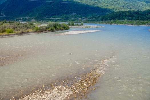 landscape with mountain river among spruce forest. beautiful sunny morning in springtime. grassy river bank and rocks on the shore. waves above boulders in the water. white fluffy cloud on the sky