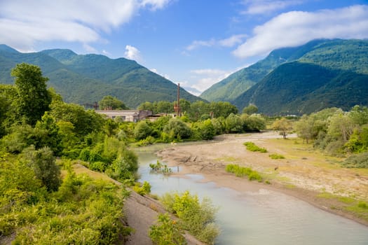landscape with mountain river among spruce forest. beautiful sunny morning in springtime. grassy river bank and rocks on the shore. waves above boulders in the water. white fluffy cloud on the sky