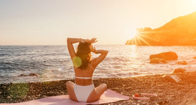 Young woman in swimsuit with long hair practicing stretching outdoors on yoga mat by the sea on a sunny day. Women's yoga fitness pilates routine. Healthy lifestyle, harmony and meditation concept.