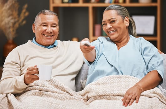 Coffee, relax and old couple watching tv with blanket on sofa in home living room laughing at comic film. Retirement portrait, valentines love and happy elderly man and woman streaming on television