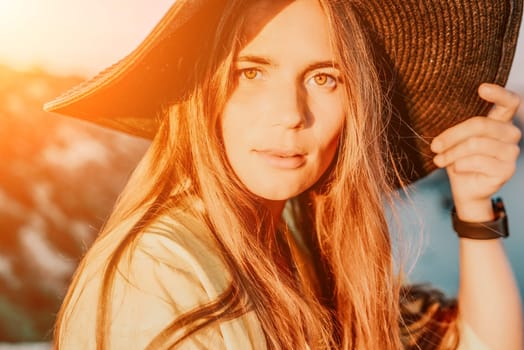 Portrait of happy young woman wearing summer black hat with large brim at beach on sunset. Closeup face of attractive girl with black straw hat. Happy young woman smiling and looking at camera at sea