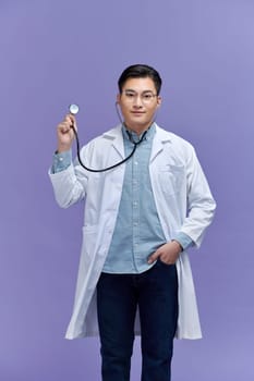 Handsome young medic holding a stethoscope, isolated over purple