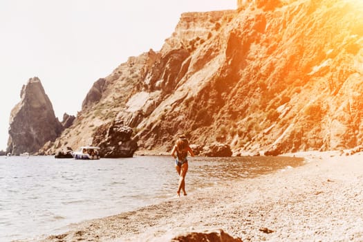 Woman travel summer sea. A happy tourist in a blue bikini enjoying the scenic view of the sea and volcanic mountains while taking pictures to capture the memories of her travel adventure