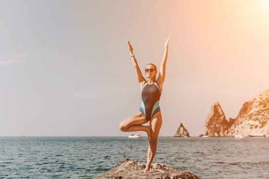 Yoga on the beach. A happy woman meditating in a yoga pose on the beach, surrounded by the ocean and rock mountains, promoting a healthy lifestyle outdoors in nature, and inspiring fitness concept