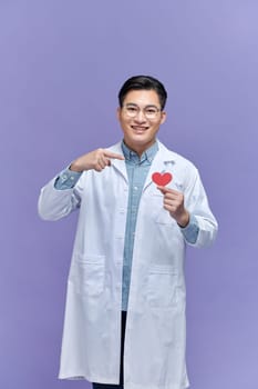 Handsome young doctor man holding paper with red heart, very happy pointing with hand and finger