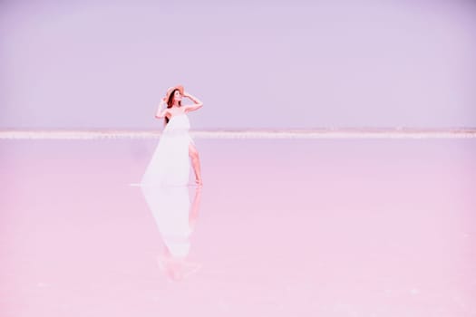 Woman in pink salt lake. She in a white dress and hat enjoys the scenic view of a pink salt lake as she walks along the white, salty shore, creating a lasting memory