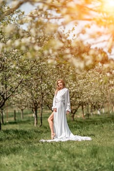 Blond blooming garden. A woman in a white dress walks through a blossoming cherry orchard. Long dress flies to the sides