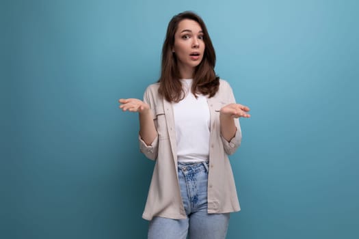 confused young dark-haired lady in informal clothes on a blue background.