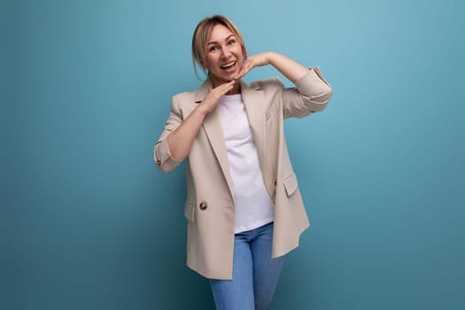 charming blonde young adult in jacket smiling on studio background.